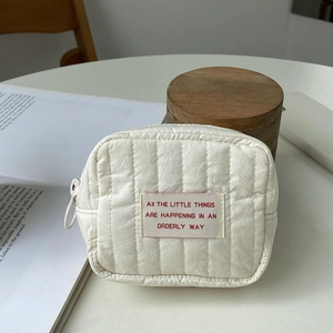 Close-up of white quilted cosmetic mini bag with pink label on a wooden desk