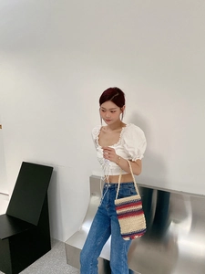 Close-up of woven straw shoulder bag with colorful stripes on a white puff-sleeve top