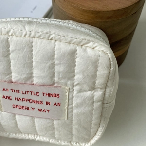 Close-up of cream quilted cosmetic bag with vertical stitching and woven label detail