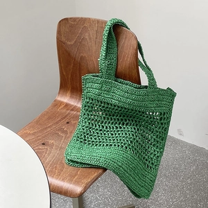 Bolso tote de paja tejida verde con diseño calado colgado en una silla de madera