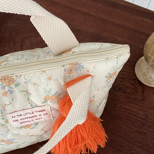 Détail du sac à lunch fleuri avec poignées beiges et décor de pompon en laine orange vif