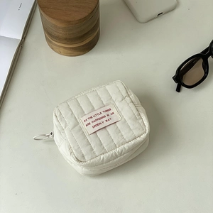 Close-up of quilted cream mini makeup bag with zip ring on lifestyle background