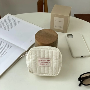 Close-up of cream quilted mini cosmetic bag featuring a red inspirational text patch