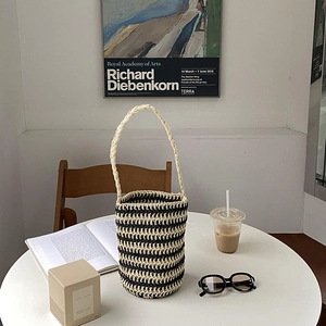 Chic black and white striped bucket straw bag with woven rope handle on a cafe table