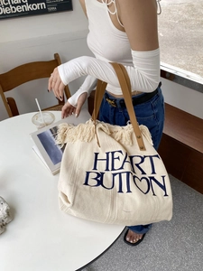 Close-up of large canvas tote bag featuring cream fringes and brown leather handles