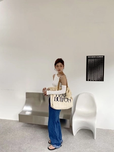 Detail of canvas fringe tote bag with blue text and leather straps in a minimalist setting