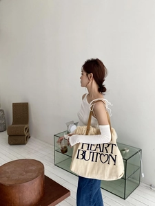 Detail view of canvas tote bag featuring fringe edges and brown leather shoulder straps