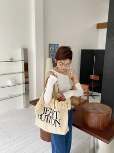 Detail of canvas tote bag featuring cream tassels, leather handles and blue text print