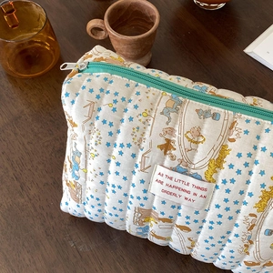 Quilted circus animal makeup bag with zipper closure on dark wood table surface