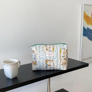 Detailed view of a quilted cotton pouch with bear prints and a green zipper on a display stand