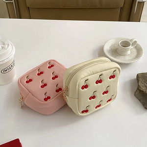 Détail de trousses à maquillage en velours rose et crème avec broderie cerise rouge