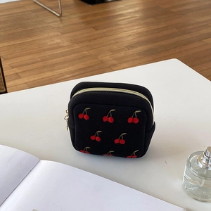 Détail d'une pochette noire en toile avec broderie cerise rouge et zip doré élégant