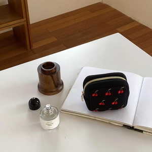 Détail de la pochette à cosmétiques noire avec broderie cerise rouge et zip doré
