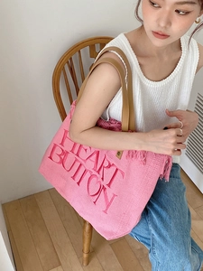 Detail view of pink canvas tote with fringe trim and brown leather handles on a model