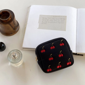 Détail d'une pochette noire en tissu avec broderie cerise rouge et fermeture dorée