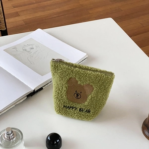 Close-up of green teddy fleece makeup bag with happy bear embroidery and metal zipper