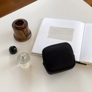 Gros plan de la pochette à bijoux noire carrée avec zip doré sur un bureau blanc minimaliste
