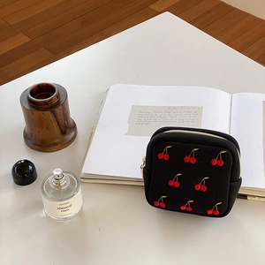 Gros plan de la pochette à bijoux noire avec broderie cerise et fermeture dorée