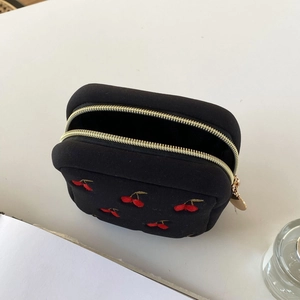 Vue détaillée d'une trousse à maquillage noire brodée de cerises avec fermeture éclair dorée