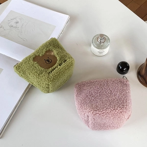 Close-up of plush green and pink teddy bear makeup bags with embroidery on a desk