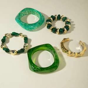 Detail of green resin bangles and gold hammered cuffs mixed with beaded stretch bracelets