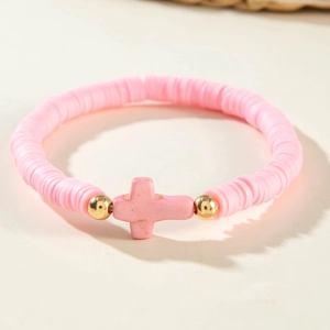 Détail d'un bracelet en perles heishi roses avec pendentif croix et accents dorés
