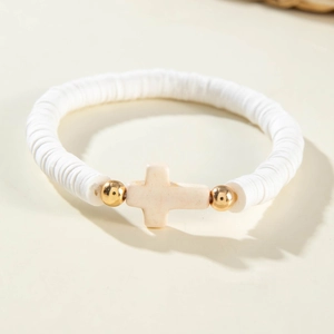 Détail d'un bracelet en perles d'argile polymère blanche avec pendentif croix beige