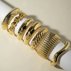Ensemble de 7 bracelets punk dorés aux textures torsadées sur présentoir blanc