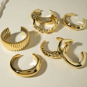 Détails de divers bracelets manchettes dorés avec des motifs ondulés et en métal torsadé