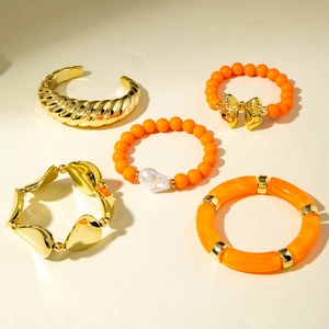 Détail d'un ensemble de cinq bracelets or et orange avec nœuds et breloques cœurs