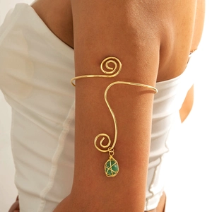 Detail of a gold spiral arm cuff featuring a wrapped green gemstone pendant on model