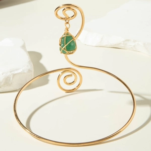 Detailed shot of golden spiral arm cuff featuring a green gemstone wire-wrapped pendant
