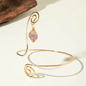 Detail view of gold spiral arm cuff with a purple raw stone pendant in a boho style