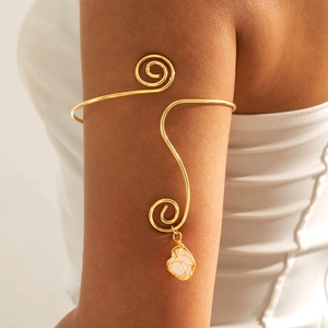 Close-up of golden spiral arm cuff featuring a delicate raw pink gemstone pendant
