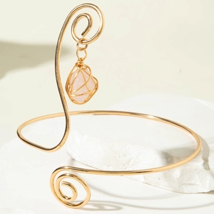 Detailed shot of golden spiral arm cuff featuring wire-wrapped pink gemstone pendant