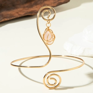 Detail of gold spiral arm cuff featuring wire-wrapped rose quartz gemstone