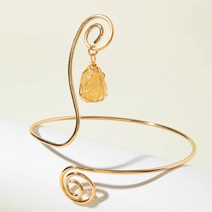 Detail of a gold spiral arm cuff featuring a wrapped yellow gemstone on a white stand
