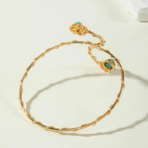 Macro detail of gold coiled wire arm cuff featuring turquoise bead accents on the ends