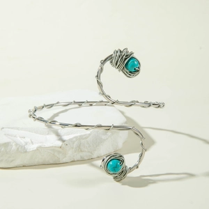 Detail of silver spiral arm cuff featuring turquoise stones on a white stone base