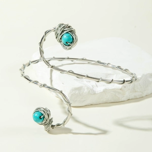 Detailed close-up of spiral woven silver arm cuff with turquoise beads on stone