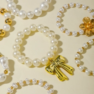 Layered white pearl bracelet set with gold bow and flower charms on a beige backdrop