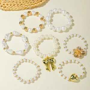 Multi-layer pearl bracelet set with gold bow flower heart charms on beige background