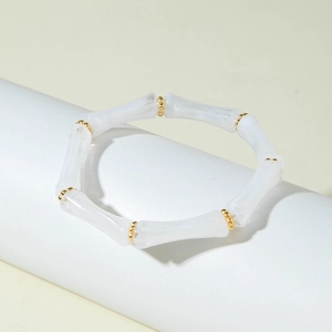Dettaglio del bracciale elastico stile bambù bianco con sfere dorate su espositore