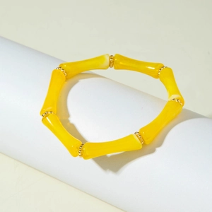Dettaglio del bracciale a tubo di bambù in acrilico giallo con distanziatori dorati