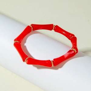 Dettaglio del braccialetto in acrilico rosso a forma di bambù con perline dorate su base