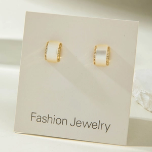 Detail of gold-plated earrings featuring white cat eye stone and pave zircon borders