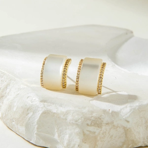Detailed macro view of square gold-plated earrings with cream stones and pavé crystals