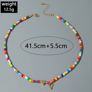 Détail du collier de perles colorées avec pendentif cœur et V doré montrant la longueur