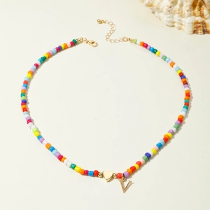 Collier de perles colorées avec pendentif cœur doré et lettre V sur fond blanc