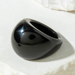 Macro detail of glossy black acrylic ring on textured stone, minimalist oval jewelry design